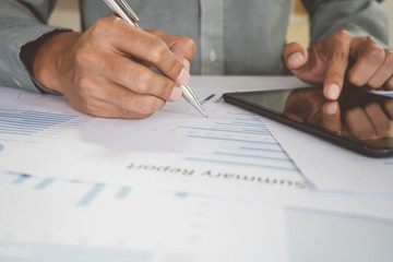 Asian businessman is using a pen to write a document report with laptop, tablet on a desk in the office. Staff checking the paper and planning the company's finances