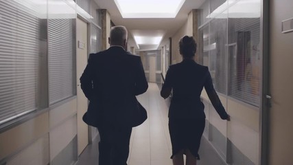 Two office workers or couple of businessmen male and female late for meeting running along corridor. Business people colleagues in formal suits run in a hurry stressed. Time is up