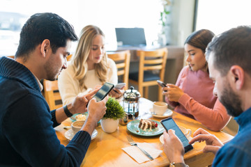 Friends Paying More Attention Towards Smartphones At Cafe