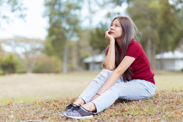 Beautiful Asian women in red dresses and blue jeans sitting in the garden. Portrait of asian woman is smiling on the green grass.