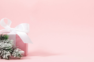 Christmas pink holiday composition. Gift with satin bow, fir tree branches on light pink pastel background. Christmas, New Year, winter concept. Front view, copy space