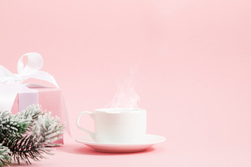 Winter or christmas pink cozy composition. Steaming cup coffee or hot drink, gift, fir tree branches on light pink pastel background. Christmas, New Year, winter concept. Front view, copy space