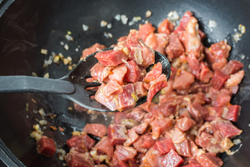 Appetizing pieces of red calf tenderloin with plastic spoon for mixing are fried in large cauldron for pilaf.