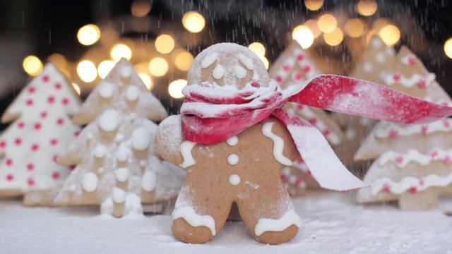 gingerbread man cookie in a red scarf with christmas trees cookies, shugar powder snow and christmas lights on a background