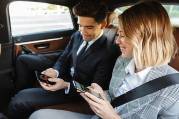 Photo of smiling man and woman using cellphones while going in car