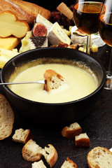 Gourmet Swiss fondue dinner on a winter evening with assorted cheeses on a board alongside a heated pot of cheese fondue with two forks dipping