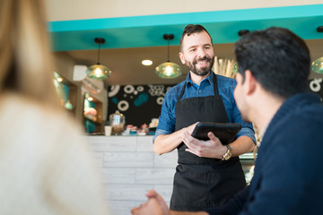 Waiter With Wireless Computer Taking Order At Restaurant