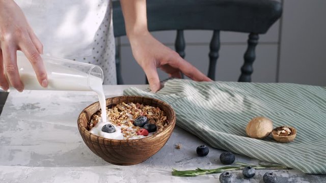 Female hand makes breakfast of granola and white yogurt in a wooden plate