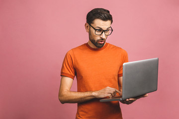 Confident business expert. Confident young amazed handsome man in casual holding laptop and smiling while standing against pink background.