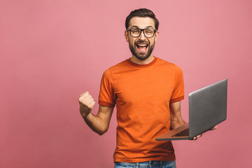 Image of happy excited young man posing isolated over pink background wall using laptop computer...