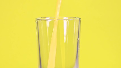Close up pouring orange juice in glass over yellow