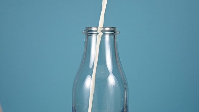 Close up pouring milk in glass bottle over blue