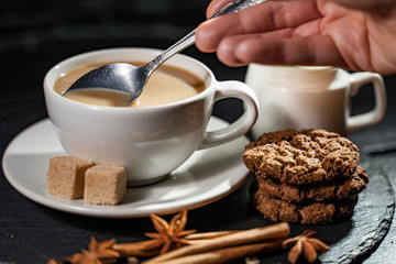 Image of a coffee cup being stirred by a white human hand, on a wooden table top