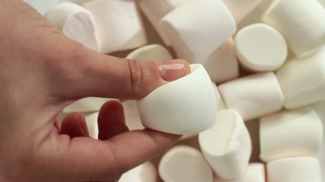 young woman holding a white marshmallow with white marshmallows on background