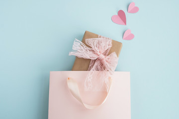 Valentines day and holiday concept. Gift box in shopping bag and pink hearts on pastel blue background. Minimal composition. Top view, flat lay, copy space