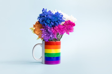 A mug painted in LGBT rainbow on a blue background as a vase, withered wilted flowers of different colors.