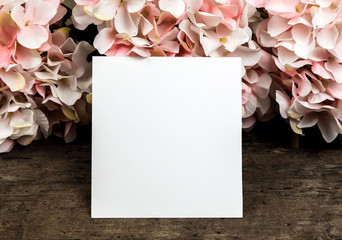 Pastel pink hydrangea flowers and a piece of paper on wood background. Copy space for text