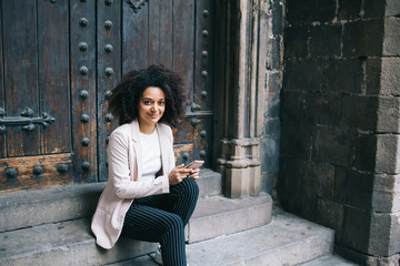 Tired black traveler with smartphone resting on stone steps