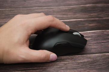 black computer mouse in hand on a wooden background. Close-up.