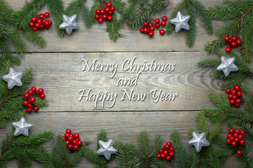 Christmas card concept with fir tree branches, rowan berries and silver glitter stars on wooden background - greeting text