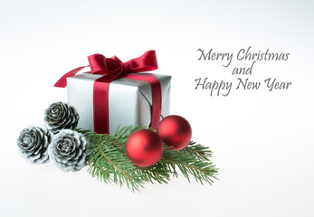 Christmas composition with a gift wrapped with red ribbon, silver cones, red baubles and a fir tree branch - isolated on white background - greetings