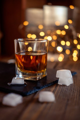 A glass of whiskey or rum with ice on a dark and bokeh background