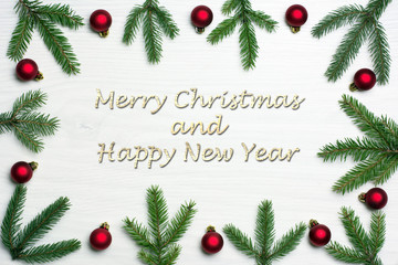 Christmas card concept with fir tree branches and red baubles on white wooden background - greetings text