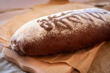 soft focus of homemade dark bread with branch print illuminated with sunlight on vintage recycling craft paper and wooden chopping board