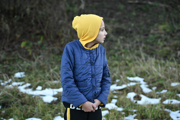 frozen little thin caucasian girl in yellow hoodie and blue jacket shiver near snow on ground in outdoor park during leisure hiking cold weather