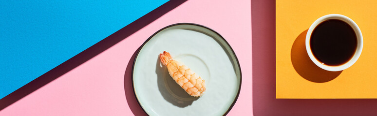 top view of fresh nigiri with shrimp near soy sauce on blue, pink, orange background, panoramic shot