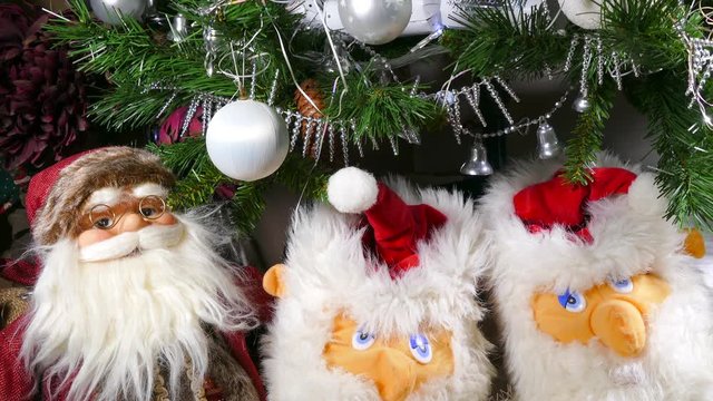 Close POV downward pan shot of an indoor Christmas tree decorated with twinking lights, tinsel and baubles, and Santa ornaments beneath.