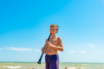 A boy plays with clarinet on the beach by the sea.