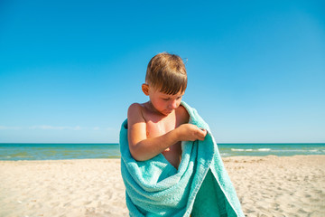 The boy on the beach hides with a towel and wipes himself from sea water after swimming in the sea.