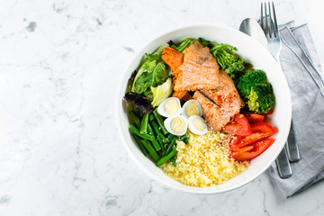 Healthy meal, keto food concept. Fish salad bowl on marble table background. Salad with salmon, couscous, vegetables, quail eggs. Top view, copy space