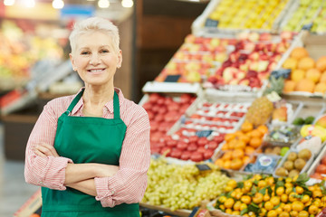 Waist up portrait of smiling senior woman looking at camera while selling fruits and vegetables at farmers market, copy space