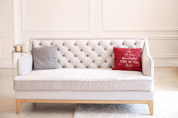 Pillow with Christmas decoration on a beige sofa in interior of room. Modern minimalist living room interior with sofa against a white wall. Spacious classic style living room with a velvet sofa. 