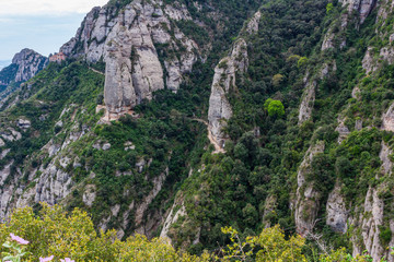 Fototapeta na wymiar View of the path that runs along the side of the cliffs to the Hermitage of St. Cova in the background, Monistrol de Monserrat, Catalonia, Spain