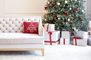 Luxury living room interior with sofa decorated chic Christmas tree, gifts and pillows. Classic interior in red shades. Christmas at home. beige sofa on background of Christmas tree.  New Year decor