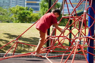 The Asian boy is climbing the robe struction toy in the park playground  at noon under sunshine.