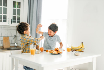 Two siblings tween boys real brothers fight at breakfast table on bright kitchen at home