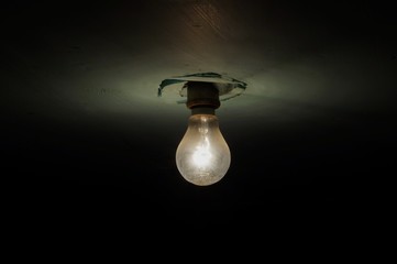 Dirty tungsten light bulb illuminated on dark background. Dusty light bulb in basement.