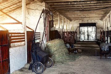 Old empty stables barn at horse farm with wooden beams , sulky cart and hay for feeding animals....