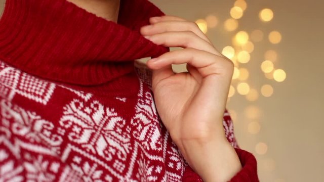 young woman wearing red and white hight neck christmas sweater with christmas lights as a background