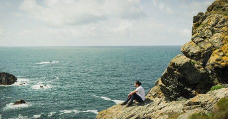 Mann sitzt nachdenklich auf Fels in Lizards Point an der Jurassic Coast, Dorset, England