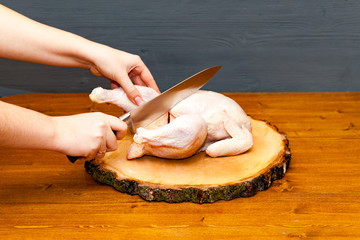Cook chef hands woman cuts carcass of whole chicken on a wooden background.