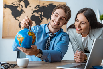 attractive travel agent standing near smiling colleague pointing with pen at globe - Powered by Adobe