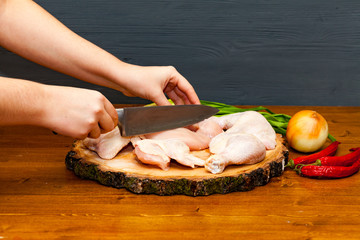 Cook chef hands woman cuts carcass of whole chicken on a wooden background.