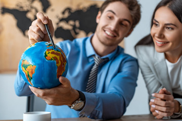 selective focus of attractive travel agent standing near smiling colleague pointing with pen at...