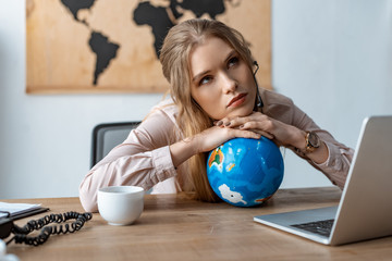 tired travel agent leaning on globe while sitting at workplace