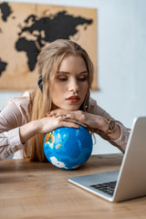 exhausted travel agent leaning on globe while looking at laptop